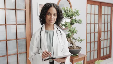 portrait of biracial female doctor wearing lab coat and stethoscope, using tablet, slow motion