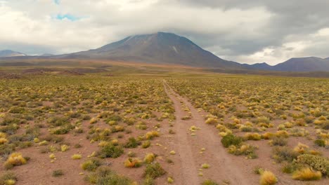 aerial action cinematic shot following a dirt road approaching a volcano in the atacama desert, chile, south america