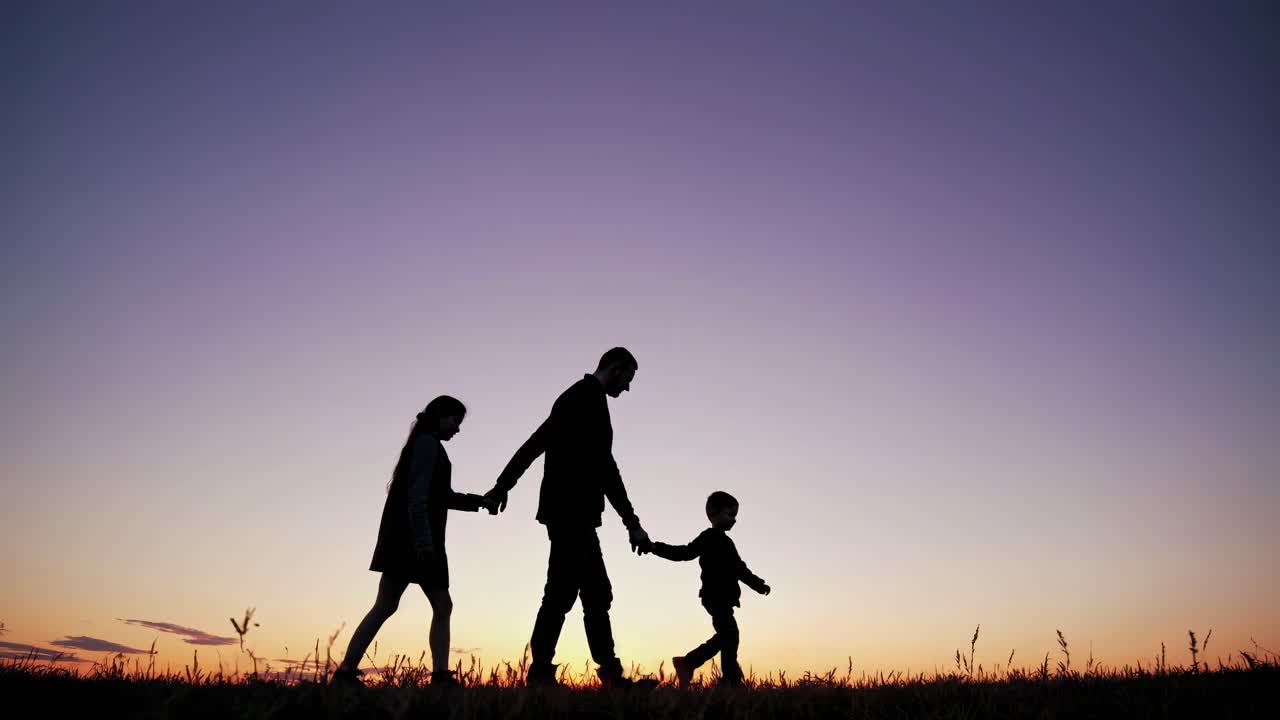 Silhouette of a family walking hand in hand at sunset, captured from a low angle