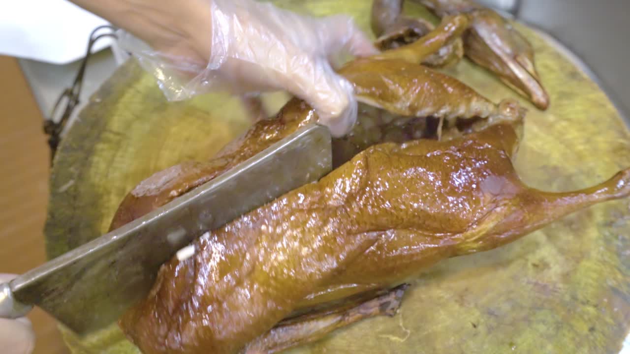 Man Cutting A Roasted Goose Into Half With A Butcher's Knife In Guangzhou, China - close up