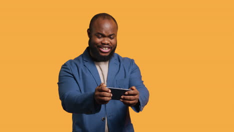 happy man playing videogames on smartphone, celebrating, studio background