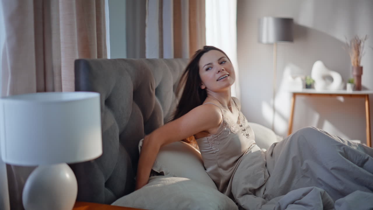 Sleepy woman stretching pillows waking up early morning closeup. Brunette lying