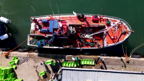 fishermen unloads fish from moored trawler at harbor, top down aerial