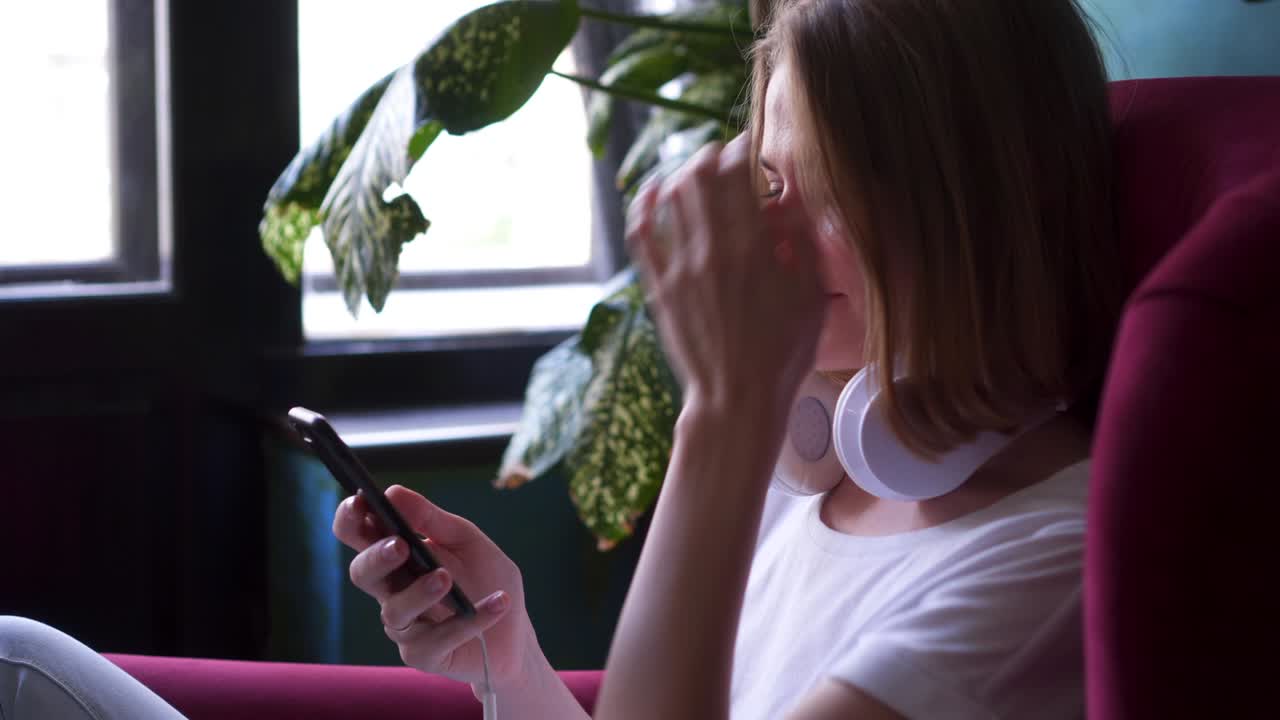 chica feliz sentada en un sillón y usando un teléfono inteligente