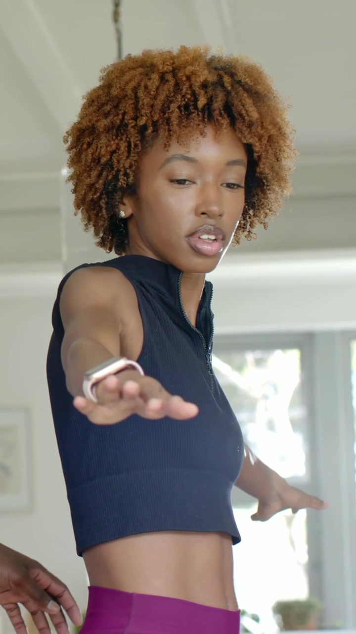 Vertical video: Balancing woman in black crop top turning at home, smartwatch and coach guiding