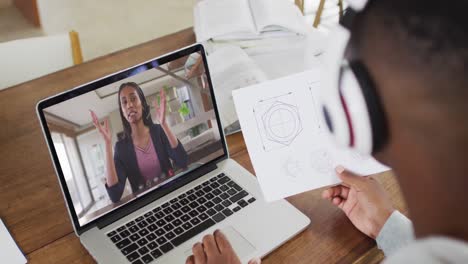 estudiante universitario afroamericano que sostiene notas mientras hace una videollamada en una computadora portátil en casa