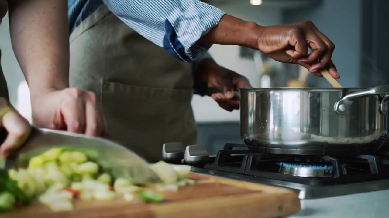Mãos de cozinheiros picando vegetais e mexendo uma panela em casa, usando aventais para cozinhar.