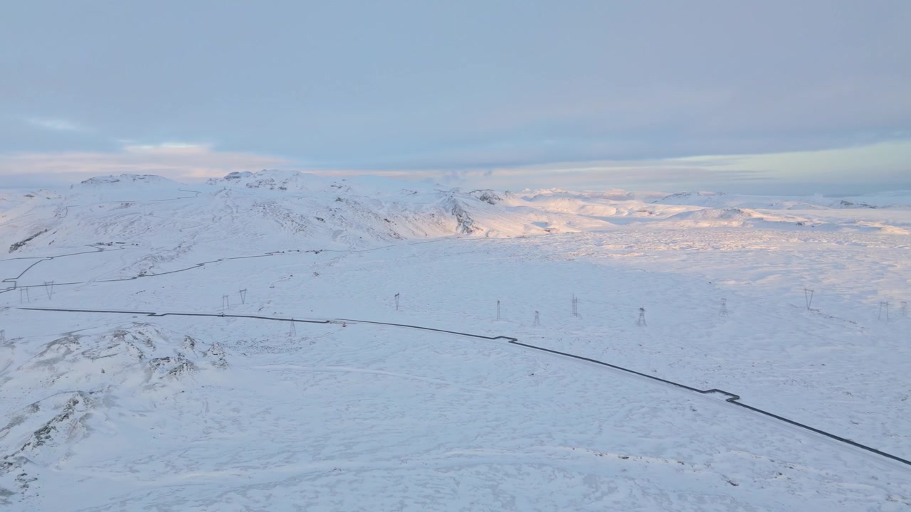 Aerial view of Icelandic highlands at dusk, mountains covered in snow, warm sunset in the background