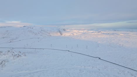 Aerial-view-of-Icelandic-highlands-at-dusk,-mountains-covered-in-snow,-warm-sunset-in-the-background