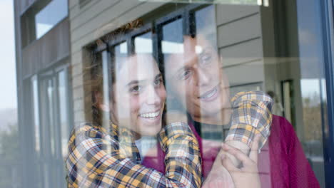 happy diverse gay male couple looking through window and embracing at home, slow motion