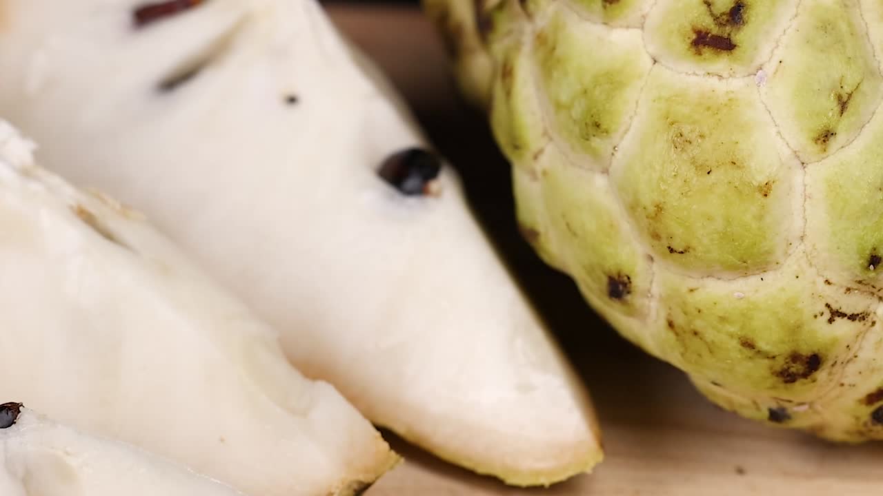 Detailed view of custard apple slices showcasing seeds and textured skin on a wooden surface.