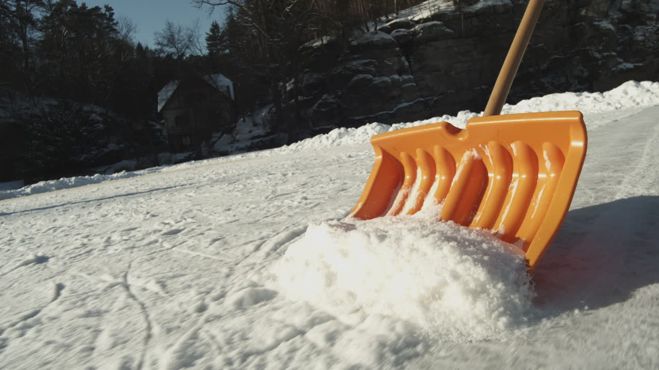 Person cleaning surface of frozen lake with snow shovel before ice skating