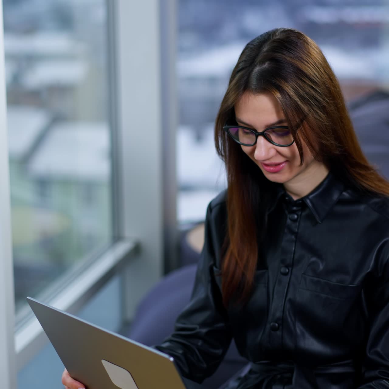 Smiling positive business lady having online chat with customers or partners. Brunette lady sits on chair looking at laptop on her knees