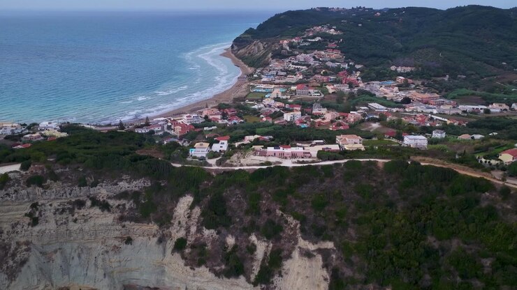 Veduta aerea con drone della spiaggia di Agios Stefanos, del villaggio costiero e delle ripide scogliere a Corfù, Grecia