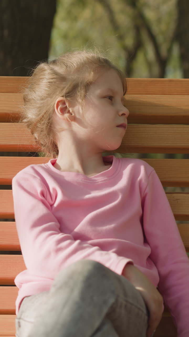 Upset little girl sits and fans away bug on bench in park closeup. Bored and offended blonde girl in spring garden. Negative emotions and feelings