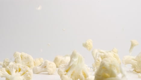 white cauliflower pieces florets bouncing on white table top in slow motion