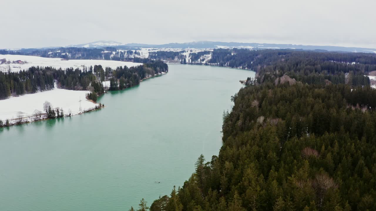 paisaje invernal de un lago turquesa rodeado de bosques y montañas cubiertos de nieve