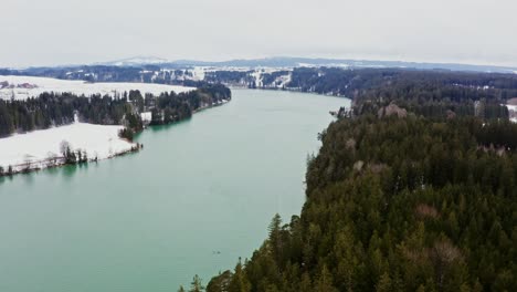 winter landscape of a turquoise lake surrounded by snow-covered forests and mountains