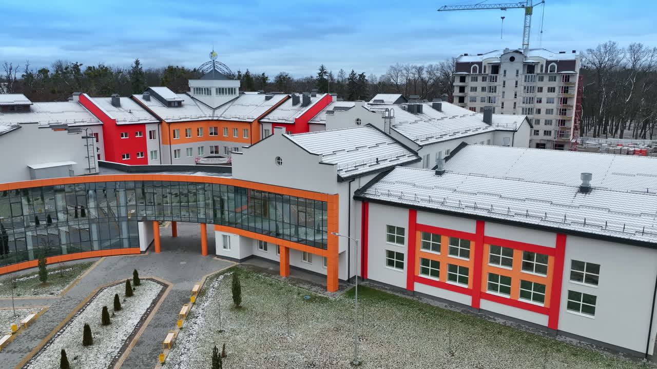 Bright exterior of a new school building. Modern architecture decisions in urban construction. Trees and apartment blocks at the backdrop.