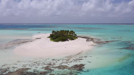 anti-clockwise orbit of small sandy island with palm trees surrounded by clear, shallow blue water and coral reef