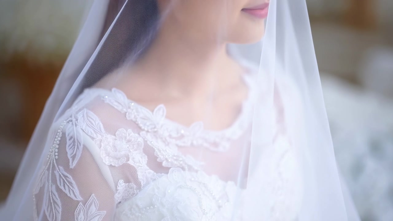 柔らかな光の中で式の準備をする若いアジア人花嫁のベールクローズアップ。レースのネックラインと優しい笑顔が印象的です。