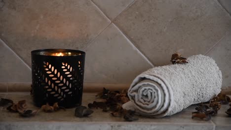 relaxing-spa-background-with-an-hidden-candle-with-flickering-flame,-some-wooden-petals-and-a-towel