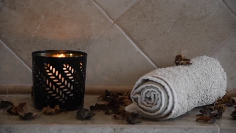 relaxing spa background with an hidden candle with flickering flame, some wooden petals and a towel