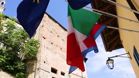 flags waving near historic buildings in cuneo, italy