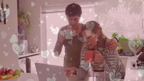 animation of hearts over caucasian female couple using laptop and drinking coffee