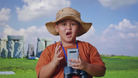 asian boy with a hat and binoculars looking at smartphone then saying wow. boy researcher examines something while traveling in stonehenge, travel tourism adventure concept, close up