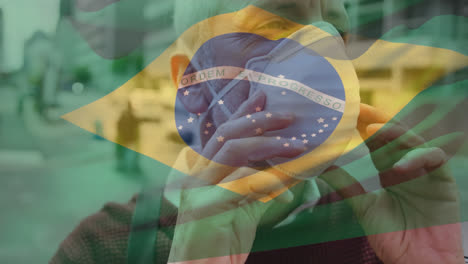 animation of flag of brazil waving over caucasian man wearing face mask in city street