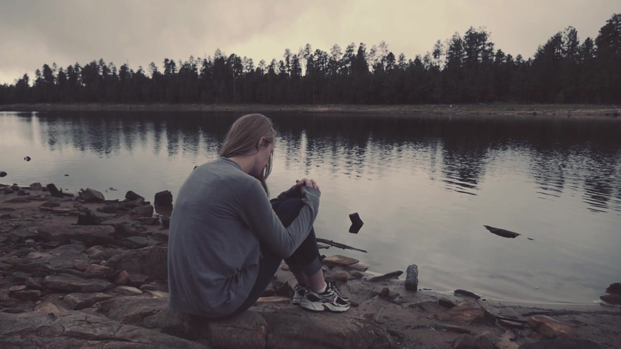 Young Woman Sitting Alone by a Lake on a Cloudy Day