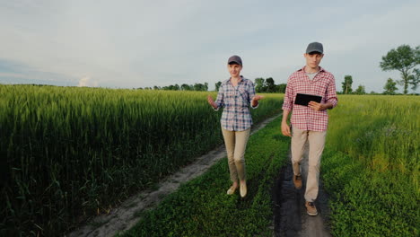 A-Couple-Of-Young-Farmers-Walk-Along-A-Country-Road-Between-Wheat-Fields