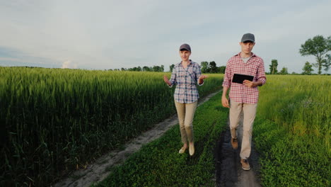 un par de jóvenes agricultores caminan por un camino rural entre campos de trigo