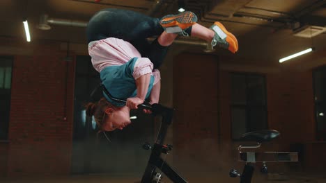 chica atlética hace trucos acrobáticos en bicicleta haciendo ejercicio en una máquina de ciclismo estacionaria en el interior