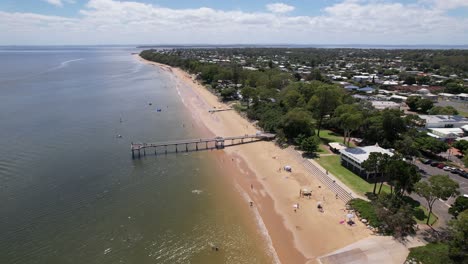 Aerial drone footage of Torquay Beach Jetty in Hervey Bay, Australia, under a bright blue summer sky