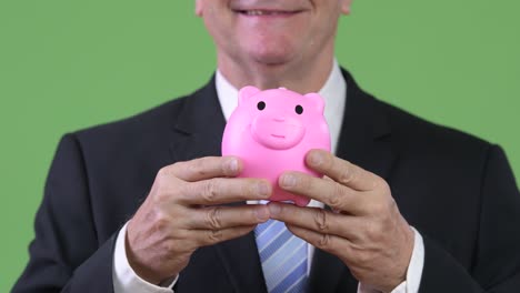 senior handsome businessman holding piggy bank