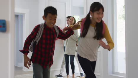 excited asian son and daughter running through front door, returning home with parents