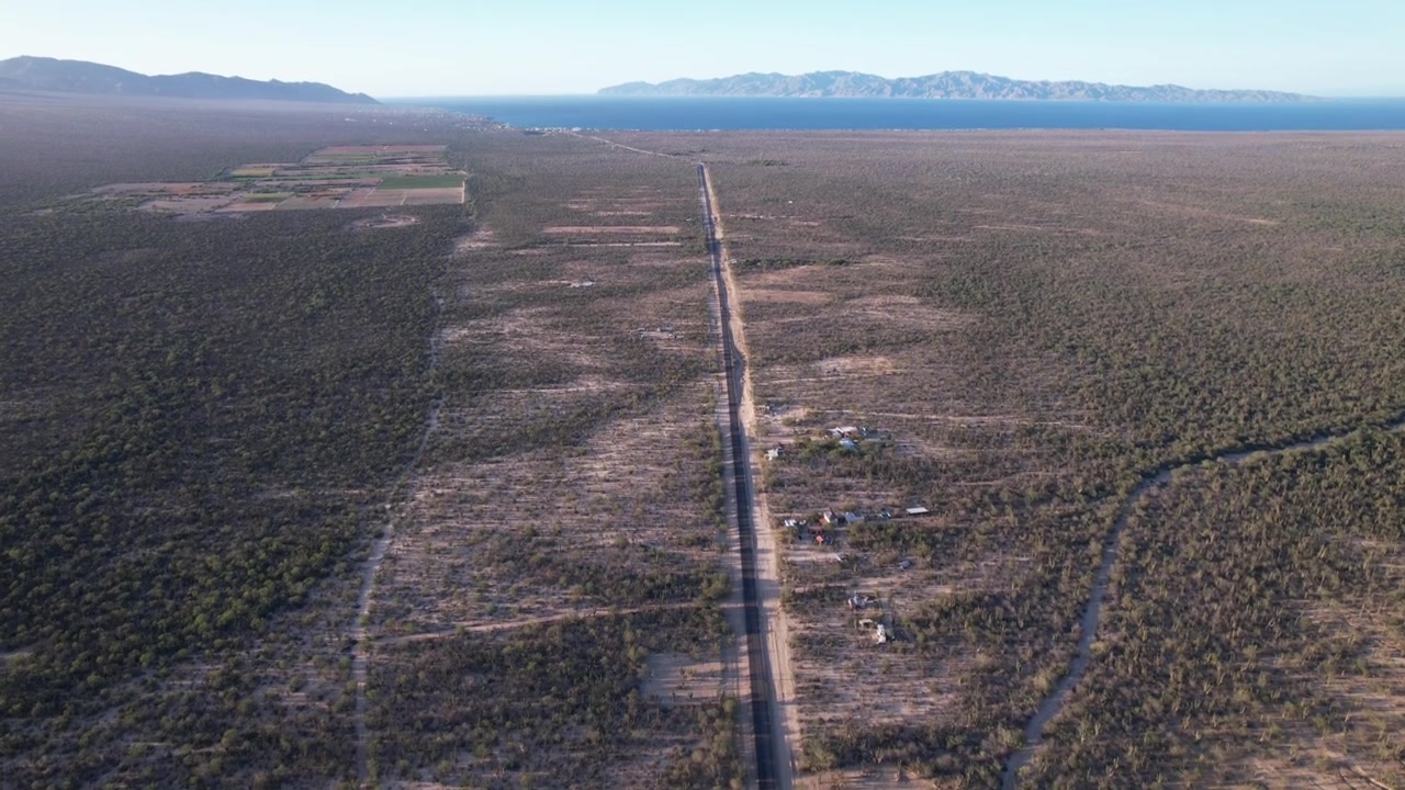 Top down aerial drone view of a straight remote road crossing a rugged desert landscape in Baja California Sur, Mexico.