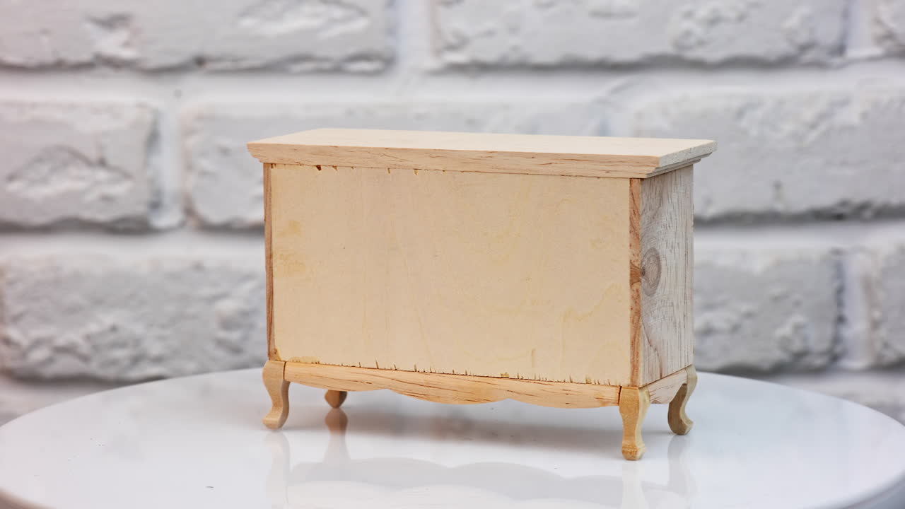 Nice little chest of drawers made from wood. Toy furniture on the rotating table. White backdrop.