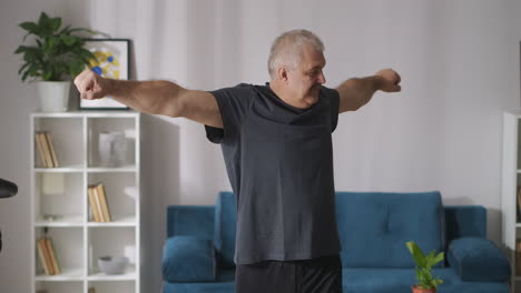 Ejercicios-Matutinos-En-Casa-Un-Hombre-Adulto-Alegre-Con-Cabello-Gris-Está-Entrenando-Solo-Gimnasia-De-Estilo-De-Vida-Saludable-Para-La-Espalda