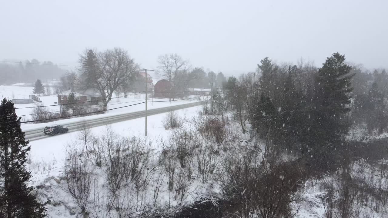 Small rural highway during a snow storm with cars driving by, aerial view