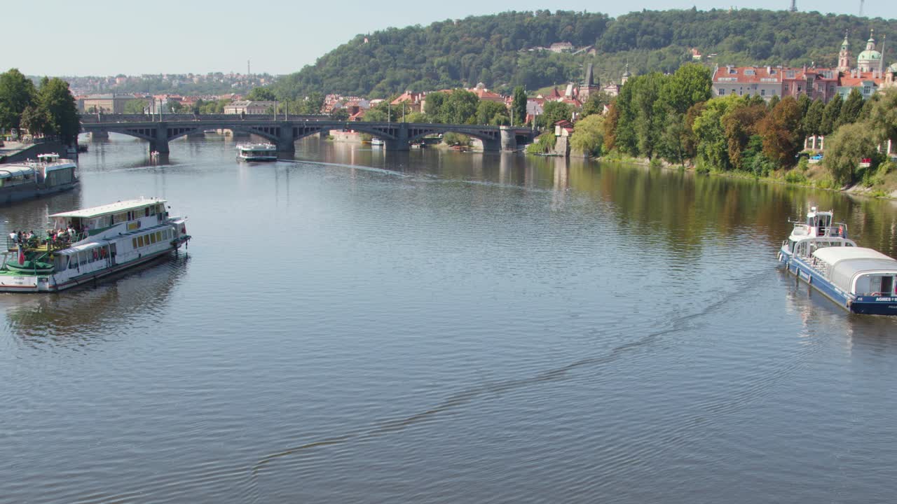 Tour boats glide along Vltava River, Prague, under bright daylight with scenic riverside architecture
