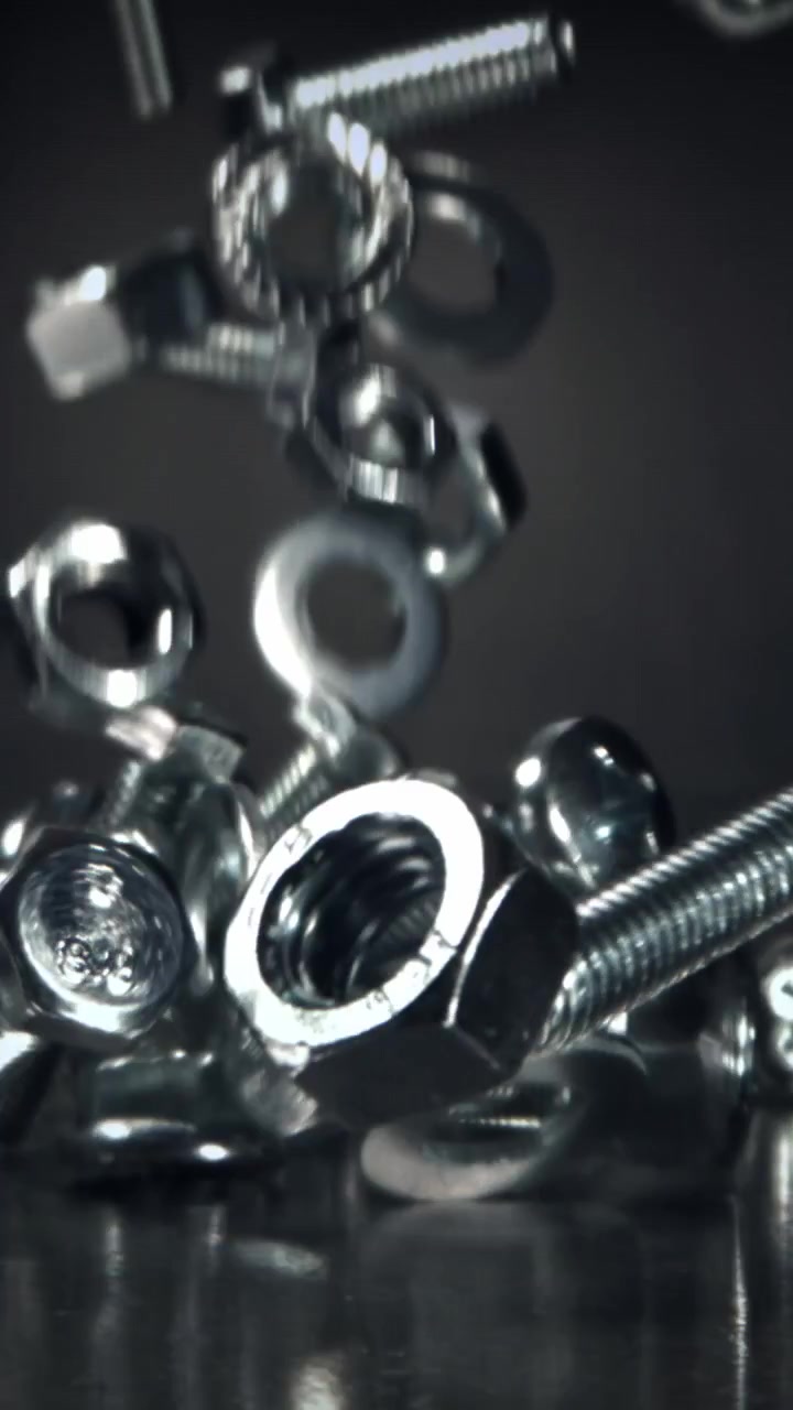 Primo piano di fissaggi metallici che cadono su una superficie scura al rallentatore
