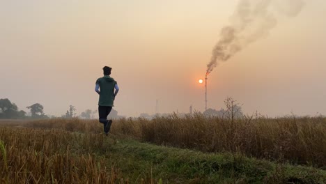 Industrial-area-with-smokestack,-man-jogging-on-rural-countryside-path,-static