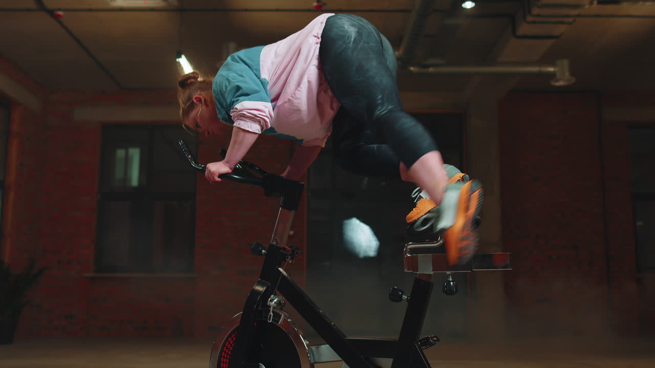 운동하는 소녀는 자전거에서 아크로바틱 트릭을 하고 실내에서 정지 자전거 기계에서 운동을 합니다.