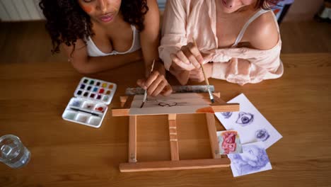Concentrated multiracial girlfriends painting together at table