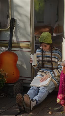 young woman reading a book outdoors by a campervan