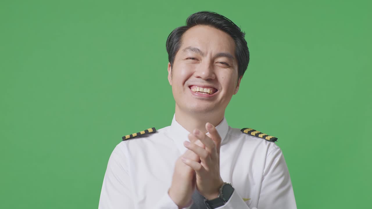 녹색 스크린 배경 스튜디오에 서 있는 동안 미소 짓고 손을 치는 아시아 남자 조종사