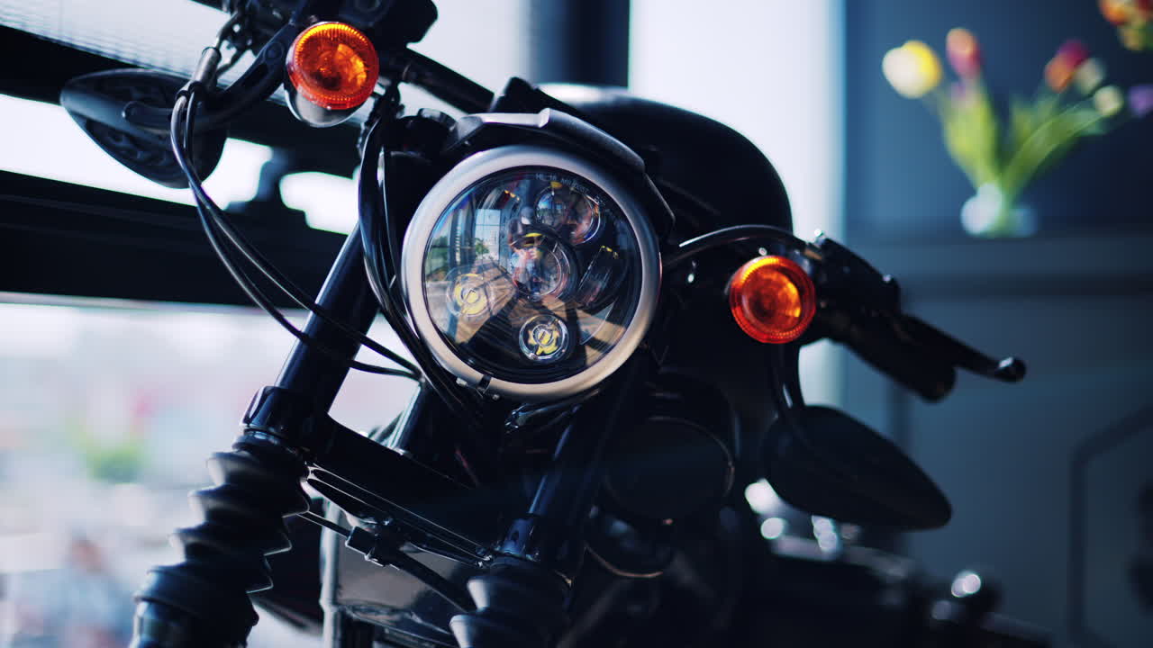 A motorcycle standing in a room next to the window with tulips on the background